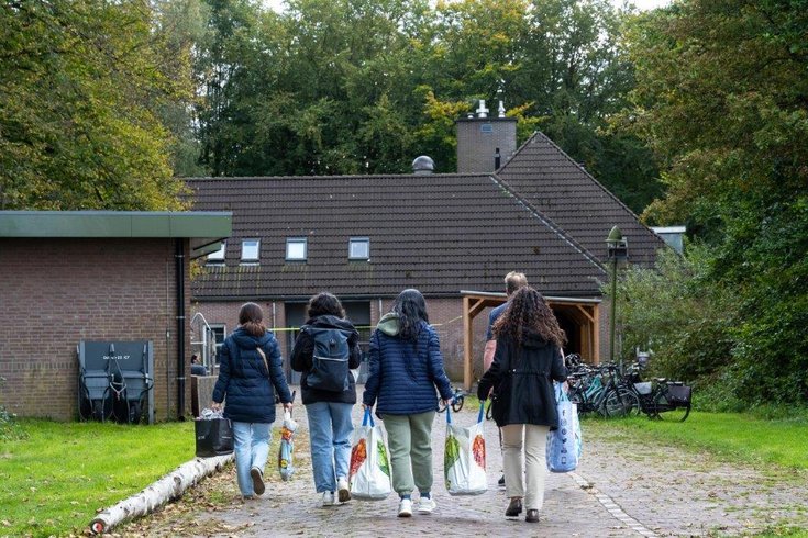 Bewoners van een opvangcentrum lopen met boodschappentassen terug naar het gebouw.