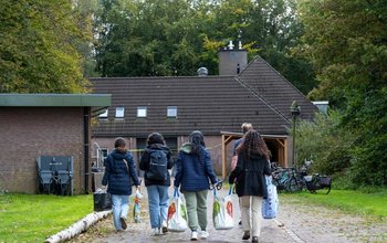 Bewoners van een opvangcentrum lopen met boodschappentassen terug naar het gebouw.