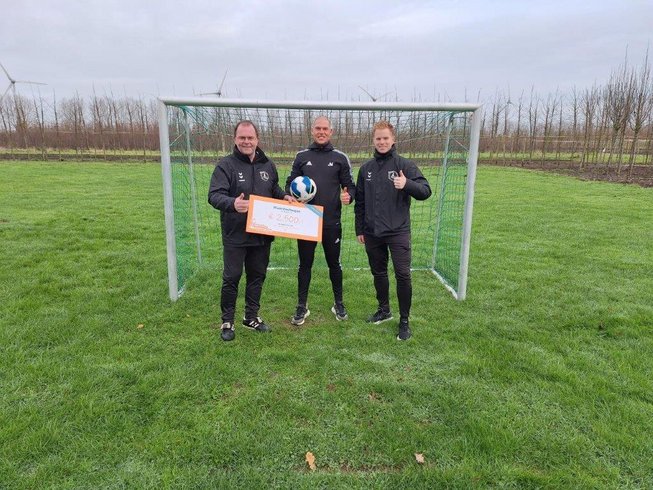 Drie personen voor een voetbal doel met een cheque van 2500 euro