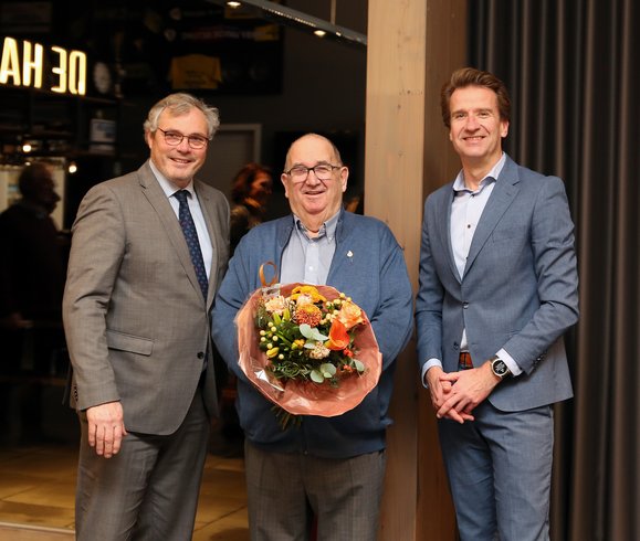 Meneer Scholz poseert met bloemen. Links van hem staat burgemeester Jan Kottelenberg en rechts wethouder René Post van Overbetuwe.
