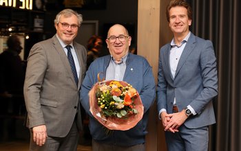 Meneer Scholz poseert met bloemen. Links van hem staat burgemeester Jan Kottelenberg en rechts wethouder René Post van Overbetuwe.