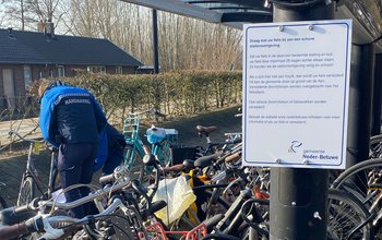 Een BOA hangt een label aan een fiets. Ook is er een bord te zien waarop staat: "Draag met uw fiets bij aan een schone stationsomgeving"