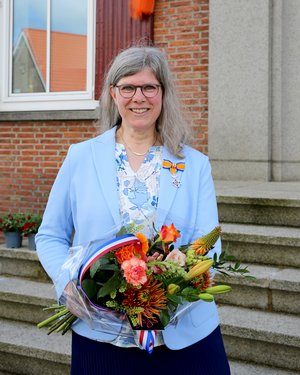 Mw. Roseboom poseert met haar onderscheiding en een bos bloemen voor het gemeentehuis.