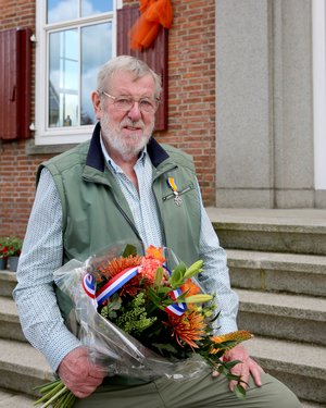 Dhr. van Kampen poseert met zijn onderscheiding en een bos bloemen voor het gemeentehuis.