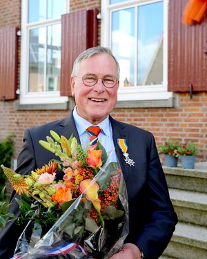 Dhr. Keuken poseert met zijn onderscheiding en een bos bloemen voor het gemeentehuis.