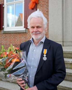 Dhr. Nieuwenhuis poseert met zijn onderscheiding en een bos bloemen voor het gemeentehuis.