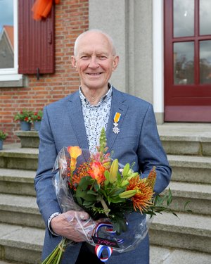 Dhr. Stoffer poseert met zijn onderscheiding en een bos bloemen voor het gemeentehuis.
