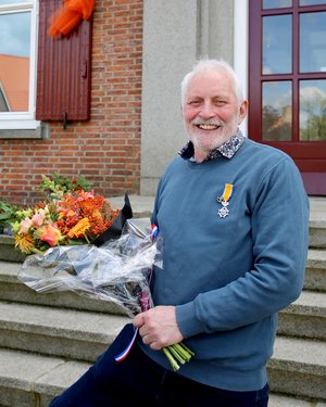 Dhr. Tijssen poseert met zijn onderscheiding en een bos bloemen voor het gemeentehuis.