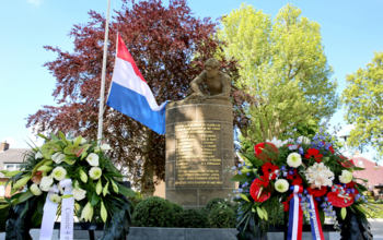 Oorlogsmonument Ochten bij de kerk met kransen en Nederlandse vlag halfstok