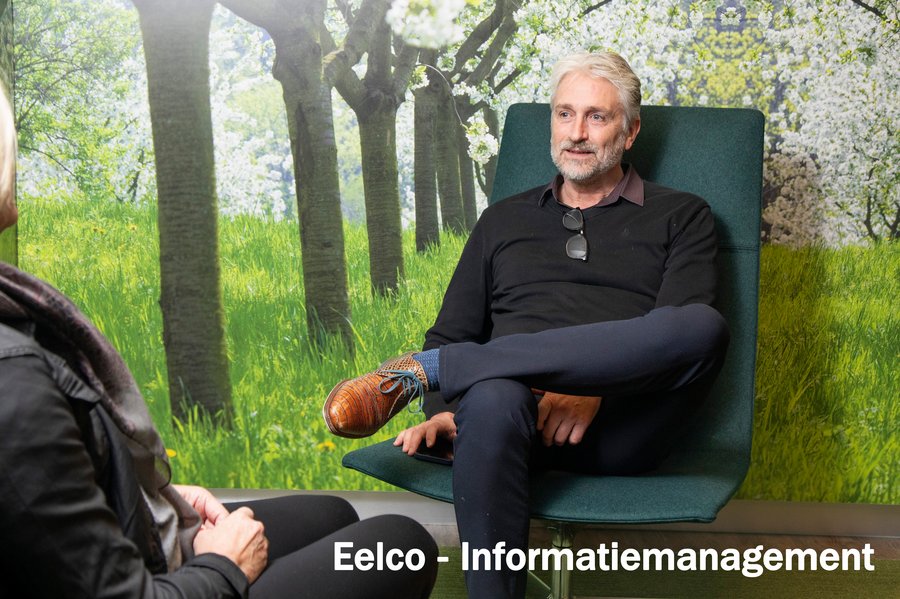 Eelco zit op een stoel met op de achtergrond een fotopapier van laanbomen in het gemeentehuis