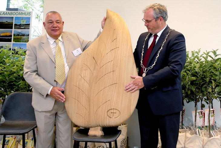 Voorzitter Goos Cardol van het Tree Centre Opheusen (links) en burgemeester Kottelenberg met het kunstwerk in de vorm van een groot houten blad bij de opening van het Laanboomhuis. Het kunstwerk is cadeau gedaan aan TCO bj de opening van het Laanboomhuis.